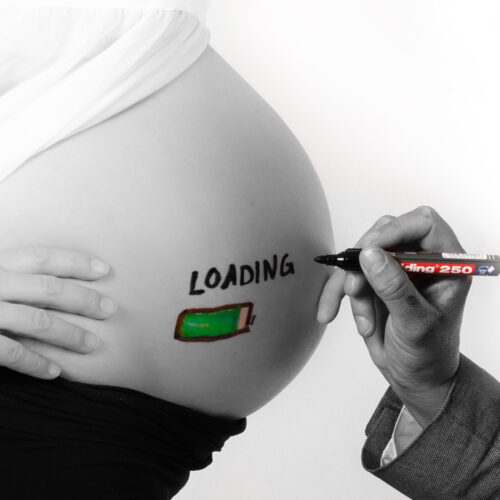 Babybauch wird angeschrieben mit grüner Loading-Batterie für das Babybauch Foto Shooting.