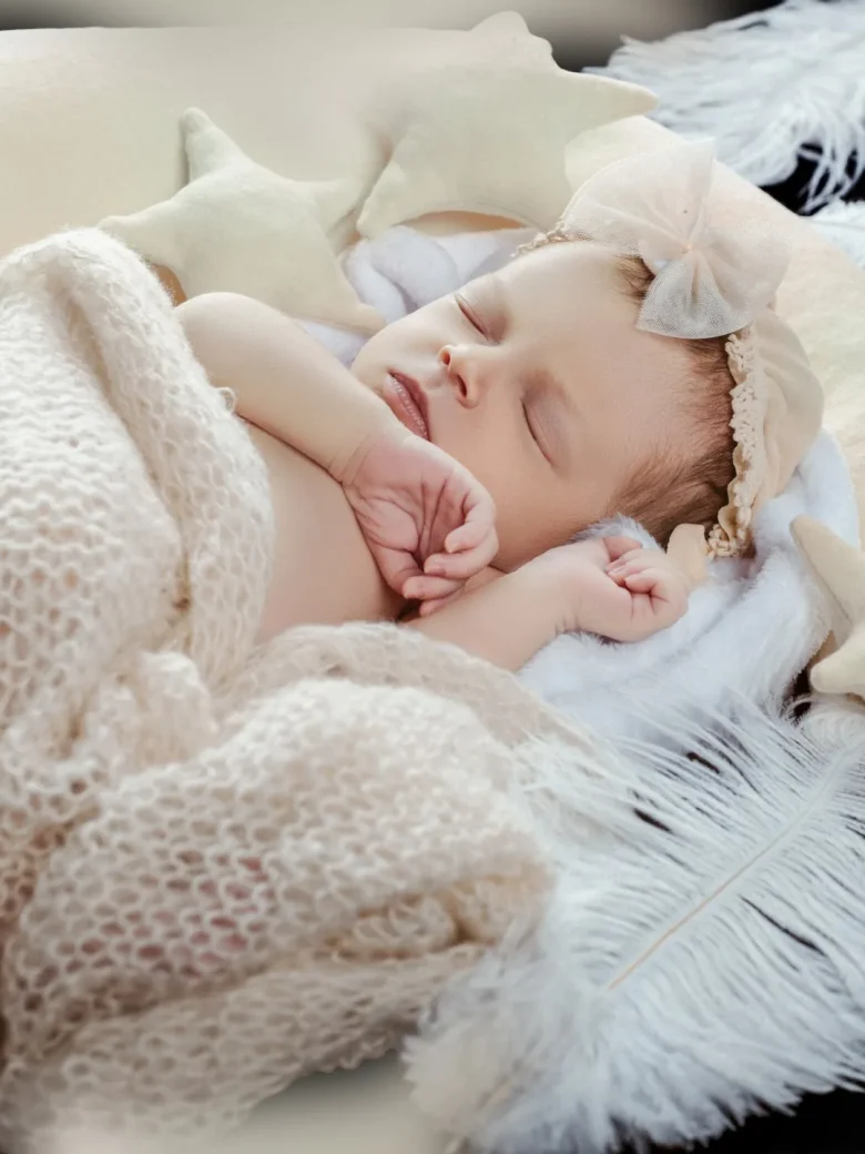 Fine-Art Newborn Fotografie – schlafendes Neugeborenes mit Schleifen-Haarband zwischen Sternkissen und weissen Federn, Studio Hitzkirch Luzern